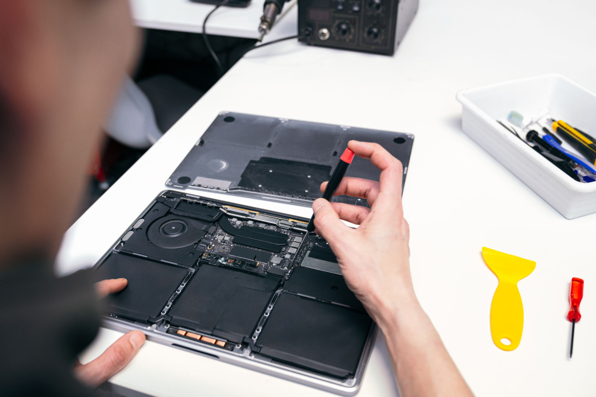 A technicians hand holding a tool over an open laptop.